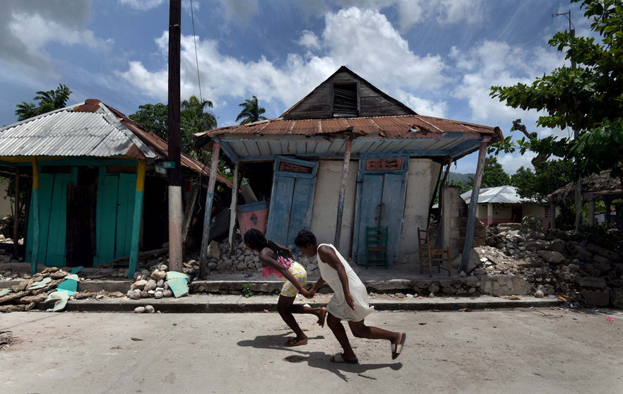 18 August 2021, Haiti, Les Cayes: Girls run in front of damaged houses after a massive earthquake in Les Cayes, Haiti. The death toll from the major earthquake that hit Haiti at the weekend has risen by almost 250 to 2,189, the country's civil defence agency said on Wednesday evening as rescue and recovery efforts continued. Photo: Carol Guzy/ZUMA Press Wire/dpa
