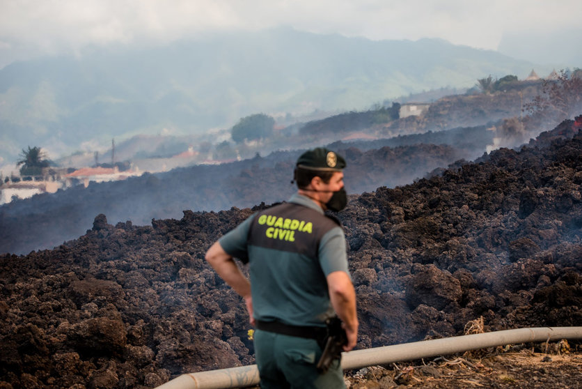 20 September 2021, Spain, El Paso: Smoke rises in front of a Guardia Civil official from cooling lava that has flowed over a road on the Canary island of La Palma. The volcano had become active again on Sunday for the first time in 50 years. Photo: Arturo Jiménez/dpa