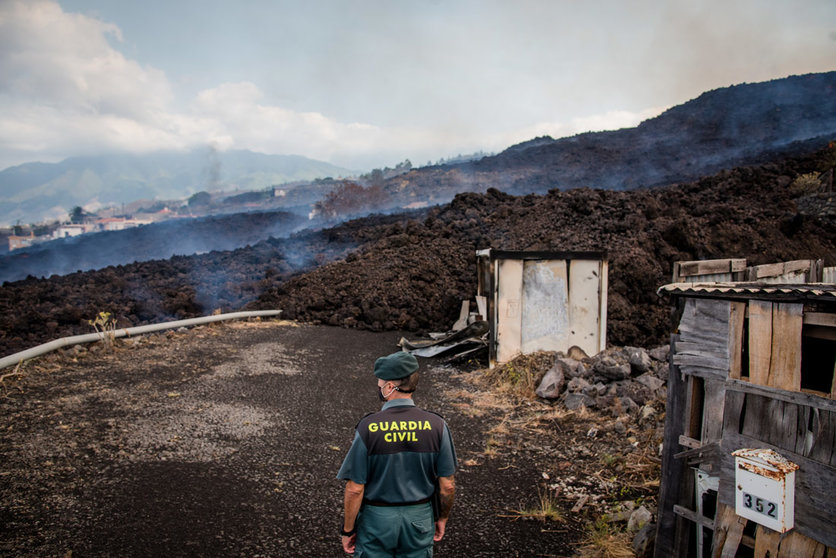 20 September 2021, Spain, El Paso: Smoke rises in front of a Guardia Civil official from cooling lava that has flowed over a road on the Canary island of La Palma. The volcano had become active again on Sunday for the first time in 50 years. Photo: Arturo Jiménez/dpa