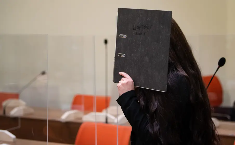 25 October 2021, Bavaria, Munich: The defendant Jennifer W. covers her face with a file in the courtroom before the trial begins. The woman who travelled to Iraq to join Islamic State has been sentenced to 10 years in jail by a court in Munich after she was charged with murder and war crimes. She allegedly stood idly by while a little Yazidi girl was chained in a courtyard and died of thirst. Photo: Sven Hoppe/dpa.