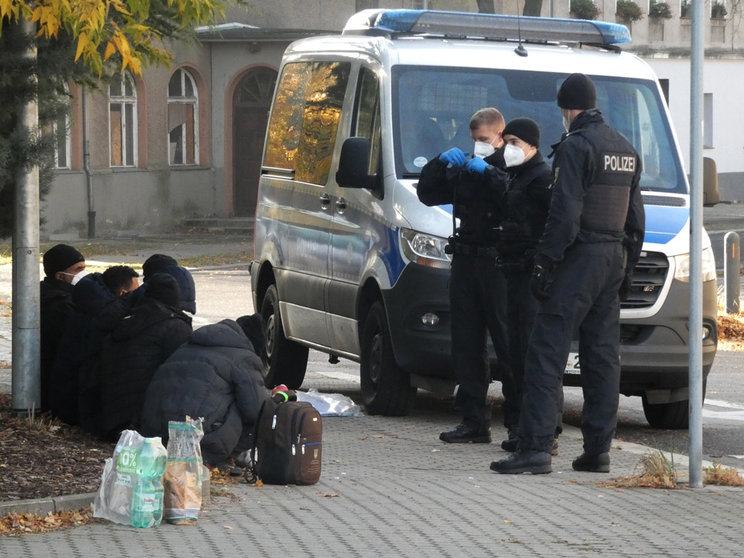 24 October 2021, Brandenburg, Guben: Federal police officers stand by a police vehicle in front of refugees who were stopped at the German-Polish border. Photo: Steil TV/dpa.