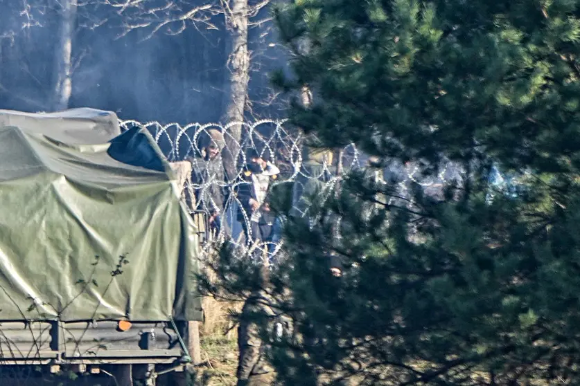 09 November 2021, Poland, Kuznica: Migrants stand behind the barbed wire border between Poland and Belarus near the Kusnica border crossing. The migration crisis at the Poland-Belarus border with refugees trying to enter the European Union via Belarus worsened on Monday, with Belarusian authorities saying that many hundreds of migrants had arrived at the border, and Poland reporting that some had already tried to break through. Photo: Michael Kappeler/dpa.