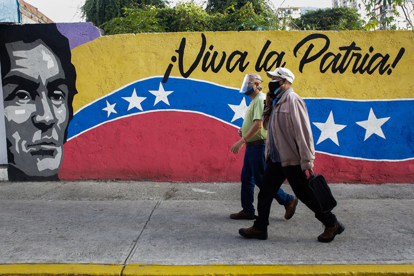 21 November 2021, Venezuela, Caracas: Two men walk in front of a mural reading "Viva la Patria" near a polling station during the local and regional elections. Photo: Stringer/dpa