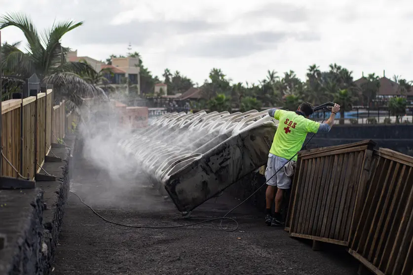 24 November 2021, Spain, La Palma: The lifeguard of a hotel on La Palma cleans the deck chairs off volcanic ash caused by the eruption of the Cumbre Vieja volcano. Photo: Pau De La Calle/EUROPA PRESS/dpa.