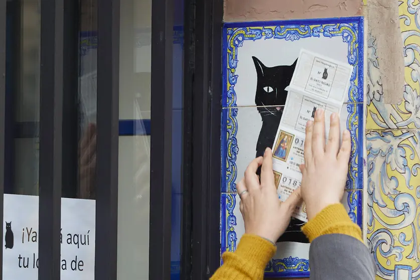 10 December 2021, Spain, Sevilla: A person rubs a Christmas Lottery ticket by the tile of the Lottery Administration El Gato Negro in Seville, a day before Spain's extraordinary Christmas lottery draw. Photo: Joaquin Corchero/EUROPA PRESS/dpa.