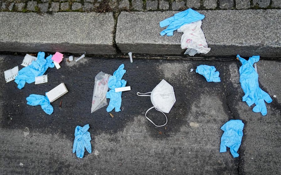 18 January 2022, Berlin: Disposable gloves, a mask and used COVID-19 rapid antigen testing kits lie on the street in front of a coronavirus test center. Photo: Kay Nietfeld/dpa.