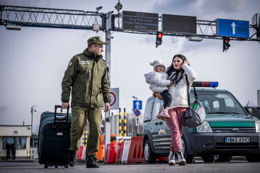 26 February 2022, Poland, Przemysl: A border guard escorts a Ukrainian refugee after she crossed the border from Shehyni in Ukraine to Medyka in Poland. Many Ukrainians leave the country after military actions by Russia on Ukrainian territory. Photo: Michael Kappeler/dpa.