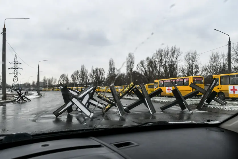 06 March 2022, Ukraine, Zaporizhzhia: Anti-tank obstacles, known as Czech hedgehogs, block a street near a convoy of buses ready to take off for besieged Mariupol to deliver humanitarian aid and evacuate people. Photo: -/Ukrinform/dpa.