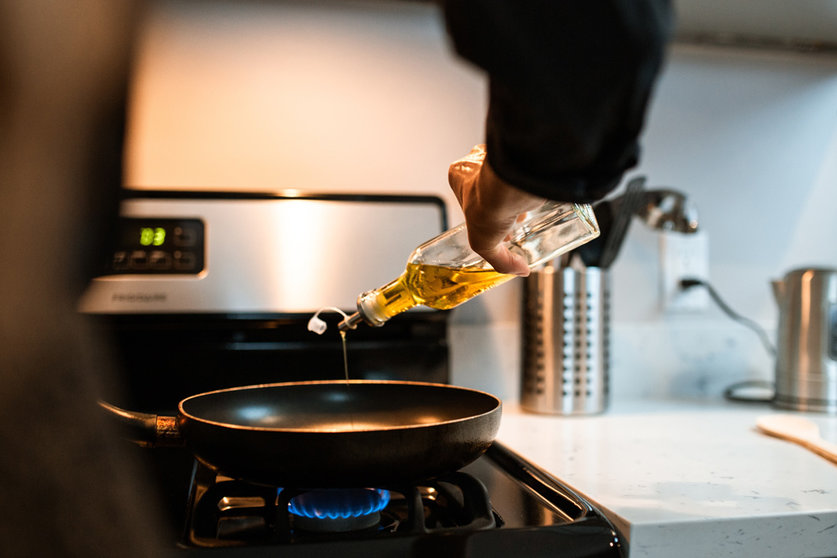 A person pouring oil into a frying pan. Photo: Pexels.