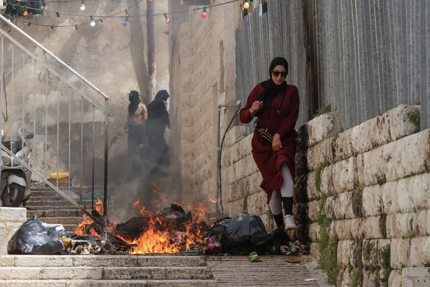 17 April 2022, Israel, Jerusalem: A Palestinian woman walks next to burning rubbish during clashes with Israeli security forces in the old city of Jerusalem. Photo: Ilia Yefimovich/dpa.