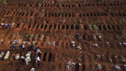 Gravediggers wearing protective suits bury the coffin of a person who died from the coronavirus disease (COVID-19), as open graves are seen at Vila Formosa cemetery, Brazil's biggest cemetery, in Sao Paulo, Brazil, May 22, 2020. Picture taken with a drone. REUTERS/Amanda Perobelli