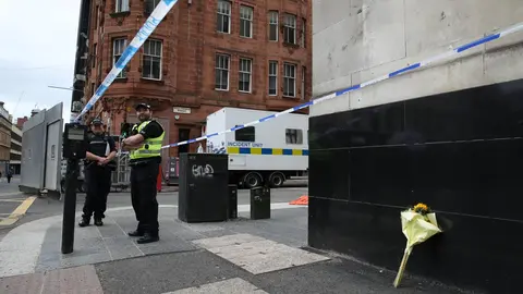 Police officers stand near a floral tribute at the crime scene on West George Street, where a man was shot Yesterday by an armed officers after another police officer was injured during an attack on Friday. Photo: Andrew Milligan/PA Wire/dpa