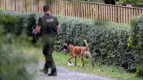 28 July 2020, Lower Saxony, Seelze: A police officer with a dog searches an area inside a garden as part of an investigation plan to find any clues about the disappearance of the British girl Madeleine McCann on 3 May 2007. Photo: Peter Steffen/dpa.