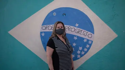 10 August 2020, Brazil, Sao Paulo: Nurse Sarah Aldana Rangon, a volunteer in a study of a possible coronavirus vaccine by Chinese pharmaceutical company Sinovac, poses with a face mask in front of a Brazilian flag painted on a wall. Photo: Andre Lucas/dpa.