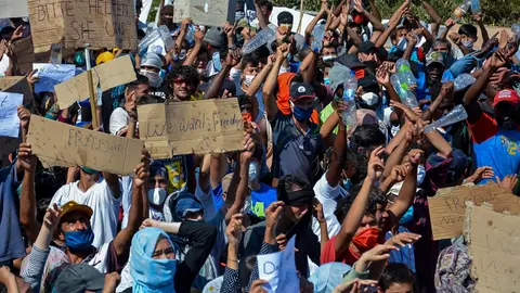 11 September 2020, Greece, Lesbos: Immigrants and refugees hold placards during a protest near the burnt-out refugee camp Moria, that was almost completely destroyed in a fire the broke out on Wednesday. More than 12,000 migrants, who lost what homes they had in the blaze that might have been intentionally set, had to spend the night on the streets. Photo: -/Eurokinissi/dpa.