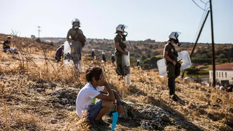 11 September 2020, Greece, Moria: A boy sits in front of policemen as migrants take part in a protest to call for their resettlement after the massive fire that burnt out the refugee camp of Moria which almost destroyed it, leaving more than 12,000 migrants homeless. Photo: Socrates Baltagiannis/dpa