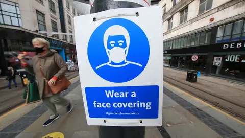 09 October 2020, England, Manchester: A woman wears a face mask passes by a sign advising on wearing face coverings near a tram stop. Cities in northern England and other areas suffering a surge in Covid-19 cases which that made many pubs and restaurants temporarily closed to combat the spread of the virus. Photo: Danny Lawson/dpa.