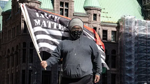12 March 2021, US, Minneapolis: A man waves the flag of black live matters while standing outside the Hennepin County Courthouse during the trial of former Minneapolis Police officer Derek Chauvin who's involved in the death of George Floyd on 25 May 2020. The family of Floyd has reached a 27 US million dollars settlement with the city of Minneapolis in a civil lawsuit over his death. Photo: Glen Stubbe/TNS via ZUMA Wire/dpa