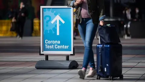 26 March 2021, Bavaria, Munich: A woman passes past a sign with the inscription "Corona Test Center" at Munich airport. A new requirement for people arriving at German airports to have submitted to coronavirus testing has been postponed from Sunday to Tuesday. Photo: Sven Hoppe/dpa