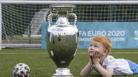 HANDOUT - 02 June 2021, United Kingdom, Glasgow: A handount pictures shows Glasgow youngster Hugo posing with the UEFA EURO 2020 Trophy as the Henri Delaunay Cup made a special visit to Glasgow on Wednesday as part of the UEFA EURO 2020 Trophy Tour. Photo: Jeff Holmes/JSHPIX via PA Wire/dpa - ATTENTION: editorial use only and only if the credit mentioned above is referenced in full