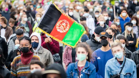 17 August 2021, Berlin: The flag of Afghanistan is held in front of the Reichstag building during a rally for a quick and unbureaucratic evacuation for threatened people from Afghanistan. Photo: Christoph Soeder/dpa
