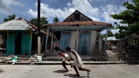 18 August 2021, Haiti, Les Cayes: Girls run in front of damaged houses after a massive earthquake in Les Cayes, Haiti. The death toll from the major earthquake that hit Haiti at the weekend has risen by almost 250 to 2,189, the country's civil defence agency said on Wednesday evening as rescue and recovery efforts continued. Photo: Carol Guzy/ZUMA Press Wire/dpa