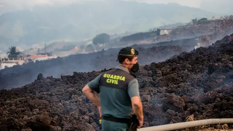 20 September 2021, Spain, El Paso: Smoke rises in front of a Guardia Civil official from cooling lava that has flowed over a road on the Canary island of La Palma. The volcano had become active again on Sunday for the first time in 50 years. Photo: Arturo Jiménez/dpa