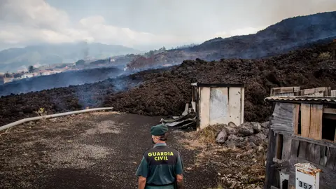 20 September 2021, Spain, El Paso: Smoke rises in front of a Guardia Civil official from cooling lava that has flowed over a road on the Canary island of La Palma. The volcano had become active again on Sunday for the first time in 50 years. Photo: Arturo Jiménez/dpa