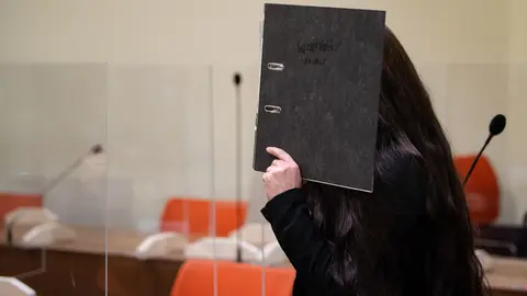 25 October 2021, Bavaria, Munich: The defendant Jennifer W. covers her face with a file in the courtroom before the trial begins. The woman who travelled to Iraq to join Islamic State has been sentenced to 10 years in jail by a court in Munich after she was charged with murder and war crimes. She allegedly stood idly by while a little Yazidi girl was chained in a courtyard and died of thirst. Photo: Sven Hoppe/dpa.