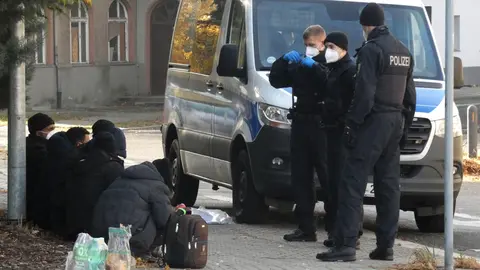 24 October 2021, Brandenburg, Guben: Federal police officers stand by a police vehicle in front of refugees who were stopped at the German-Polish border. Photo: Steil TV/dpa.