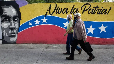 21 November 2021, Venezuela, Caracas: Two men walk in front of a mural reading "Viva la Patria" near a polling station during the local and regional elections. Photo: Stringer/dpa