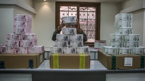 FILED - An employee piles up stacks of Turkish lira banknotes inside a bank at the northern Syrian town of Sarmada in 2020. Turkey's currency hit yet another record low of over 14 against the dollar before recouping some losses on Wednesday after a central bank move to sell reserves. Photo: Anas Alkharboutli/dpa.
