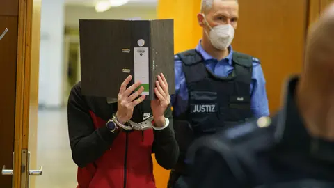 30 November 2021, Hessen, Frankfurt_Main: Iraqi defendant Taha Al-J. (L) coveres his face with a folder as he enters the courtroom of the Frankfurt's Higher Regional Court before a verdict is pronounced. The Federal Prosecution has accused Taha of genocide, crimes against humanity, war crimes, human trafficking and murder. As a suspected member of the so-called Islamic State (IS) terro group, he allegedly enslaved a Yazidi woman and her daughter and subjected them to abuse. According to the indictment, Taha faces accusations of leaving the little girl to die of thirst after tying her up in Fallujah, Iraq. Photo: Frank Rumpenhorst/dpa.