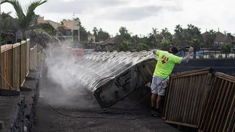 24 November 2021, Spain, La Palma: The lifeguard of a hotel on La Palma cleans the deck chairs off volcanic ash caused by the eruption of the Cumbre Vieja volcano. Photo: Pau De La Calle/EUROPA PRESS/dpa.