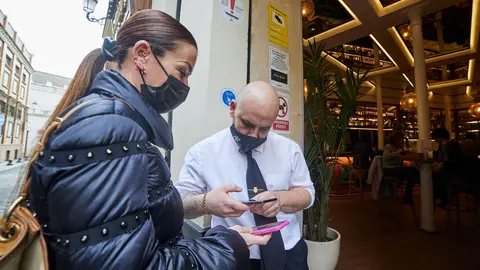 20 December 2021, Spain, Sevilla: Customers show a waiter their Corona certificates before entering a bar in Sevilla. Starting on Monday, only customers who are vaccinated, recovered or have a negative test result will be allowed into bars, restaurants, and hotels in Andalusia. Photo: Joaquin Corchero/EUROPA PRESS/dpa