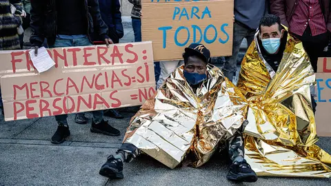 18 December 2021, Spain, Madrid: Demonstrators sit on the ground during a rally in the Plaza Juan Goytisolo on the occasion of Migrants Day. Photo: Carlos Luján/EUROPA PRESS/dpa.