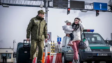 26 February 2022, Poland, Przemysl: A border guard escorts a Ukrainian refugee after she crossed the border from Shehyni in Ukraine to Medyka in Poland. Many Ukrainians leave the country after military actions by Russia on Ukrainian territory. Photo: Michael Kappeler/dpa.