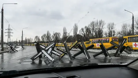 06 March 2022, Ukraine, Zaporizhzhia: Anti-tank obstacles, known as Czech hedgehogs, block a street near a convoy of buses ready to take off for besieged Mariupol to deliver humanitarian aid and evacuate people. Photo: -/Ukrinform/dpa.