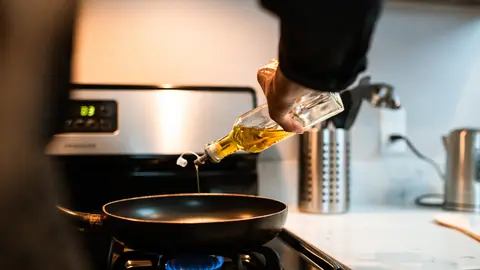 A person pouring oil into a frying pan. Photo: Pexels.