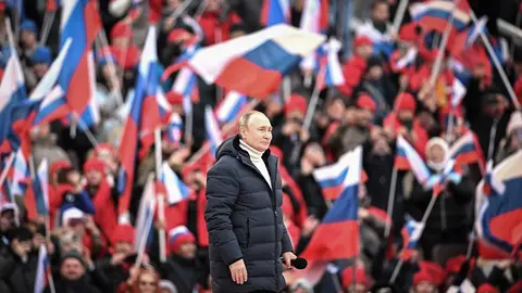 HANDOUT - 18 March 2022, Russia, Moscow: The crowd waves Russian flags as Russian President Vladimir Putin walks to deliver a speech during a concert held to mark the eighth anniversary of Russia's annexation of Crimea at the Luzhniki stadium. Photo: -/Kremlin/dpa - ATTENTION: editorial use only and only if the credit mentioned above is referenced in full.