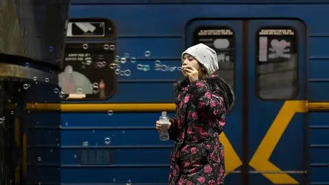 26 March 2022, Ukraine, Kiev: A young girl blows bubbles as people take shelter in a metro station serving as an underground bomb shelter. Photo: Carol Guzy/ZUMA Press Wire/dpa.
