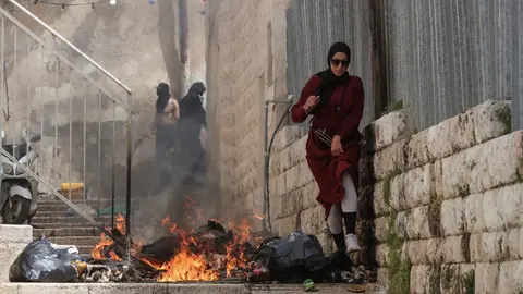 17 April 2022, Israel, Jerusalem: A Palestinian woman walks next to burning rubbish during clashes with Israeli security forces in the old city of Jerusalem. Photo: Ilia Yefimovich/dpa.
