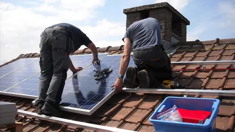 Workers placing solar panels to produce energy on a roof. Photo: Pixabay.