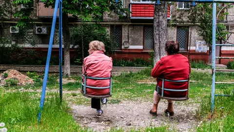 21 May 2022, Ukraine, Kramatorsk: Elderly women sit on swings in a playground in front of their damaged houses in Kramatorsk. Kramatorsk is a city in the Donetsk region known for its metallurgical industry, particularly the production of iron and steel. Photo: Rick Mave/SOPA Images via ZUMA Press Wire/dpa.