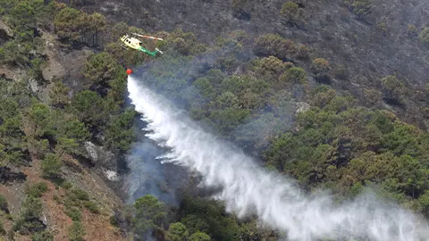10 June 2022, Spain, Pujerra: A firefighting helicopter pours water over a burned area to control a wild fire near Pujerra on the Costa del Sol. Photo: Álex Zea/EUROPA PRESS/dpa.