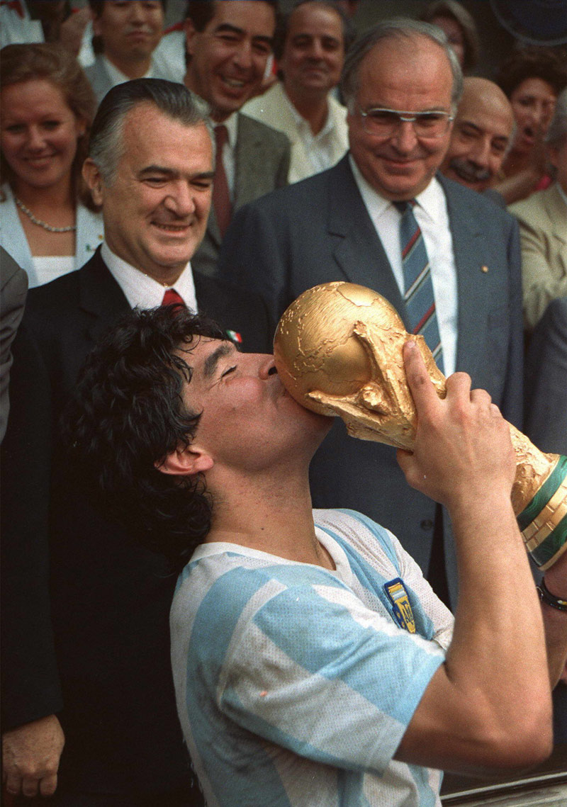FILED - 29 June 1986, Mexico, Mexico City: Argentine footballer Diego Maradona kisses the FIFA World Cup Trophy next to Mexican President Miguel de la Madrid (L) and German chancellor Helmut Kohl (R) after his team's victory over West Germany in the 1986 FIFA World Cup Final. Argentina football great Diego Maradona has died at the age of 60, the Argentinian Football Association said on Wednesday. Photo: -/dpa