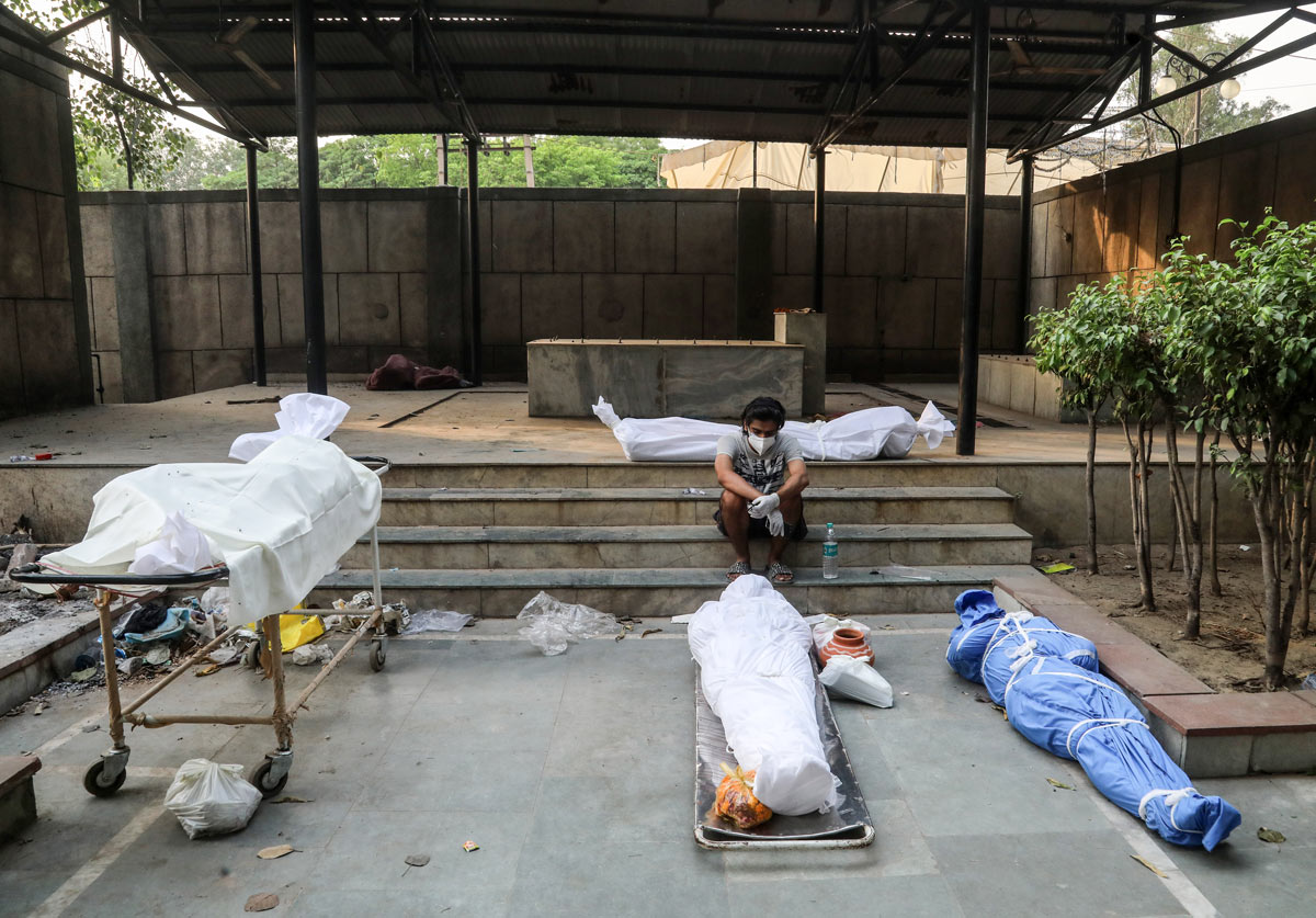 FILED - 28 April 2021, India, New Delhi: A man wearing a face mask sits next to the bodies of those who have died from the coronavirus (Covid-19) before their cremation at a crematorium in New Delhi. Photo: Naveen Sharma/SOPA Images via ZUMA Wire/dpa